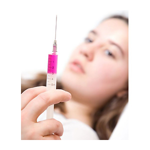 woman looking at syringe - travel jabs - holiday summer health - allaboutyou.com